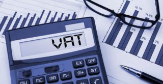 Electronic VAT calculator on desk with paperwork displaying financial graphs.